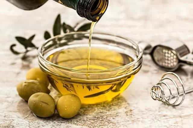 olio versato in una ciotola, con accanto delle olive verdi