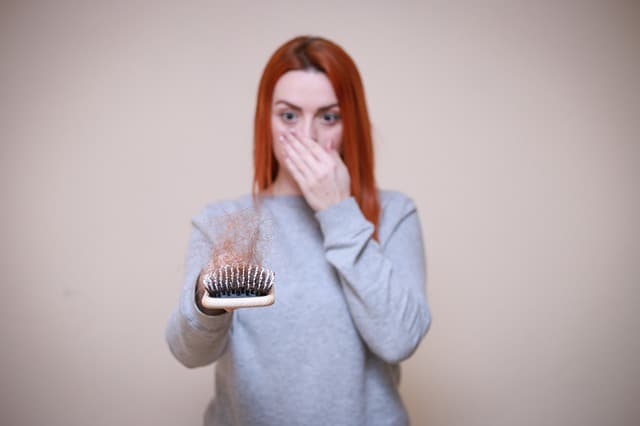una donna guarda una spazzola piena di capelli