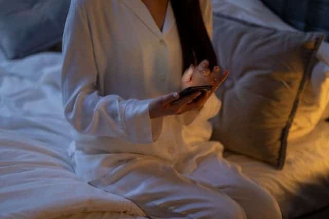 donna in pigiama con smartphone in mano si siede sul letto