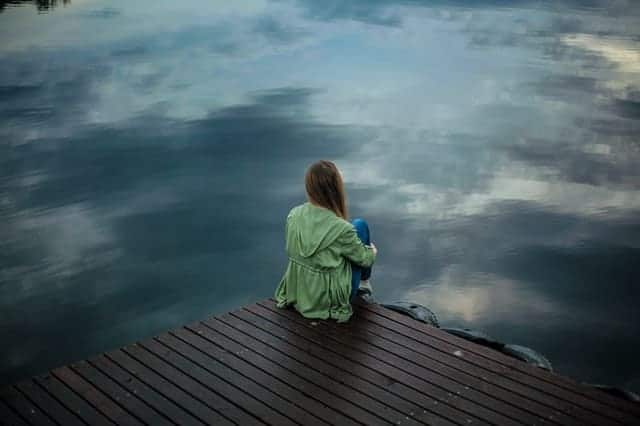  una donna si siede sul bordo di un molo e guarda nell'acqua