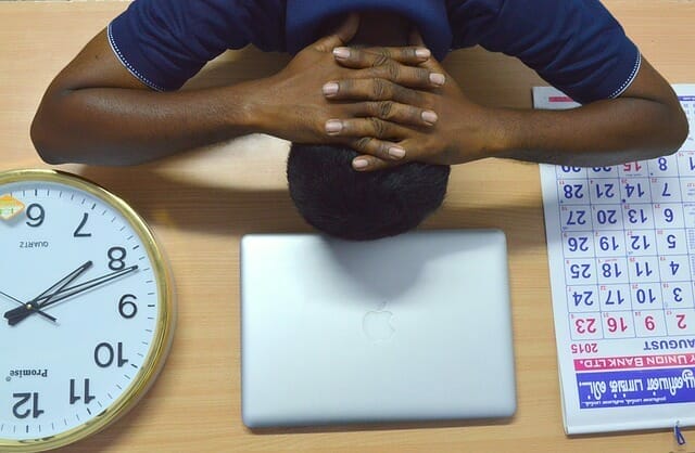  Un uomo troppo stanco tiene la testa sulla sua scrivania, accanto al suo computer portatile, al calendario e all'orologio